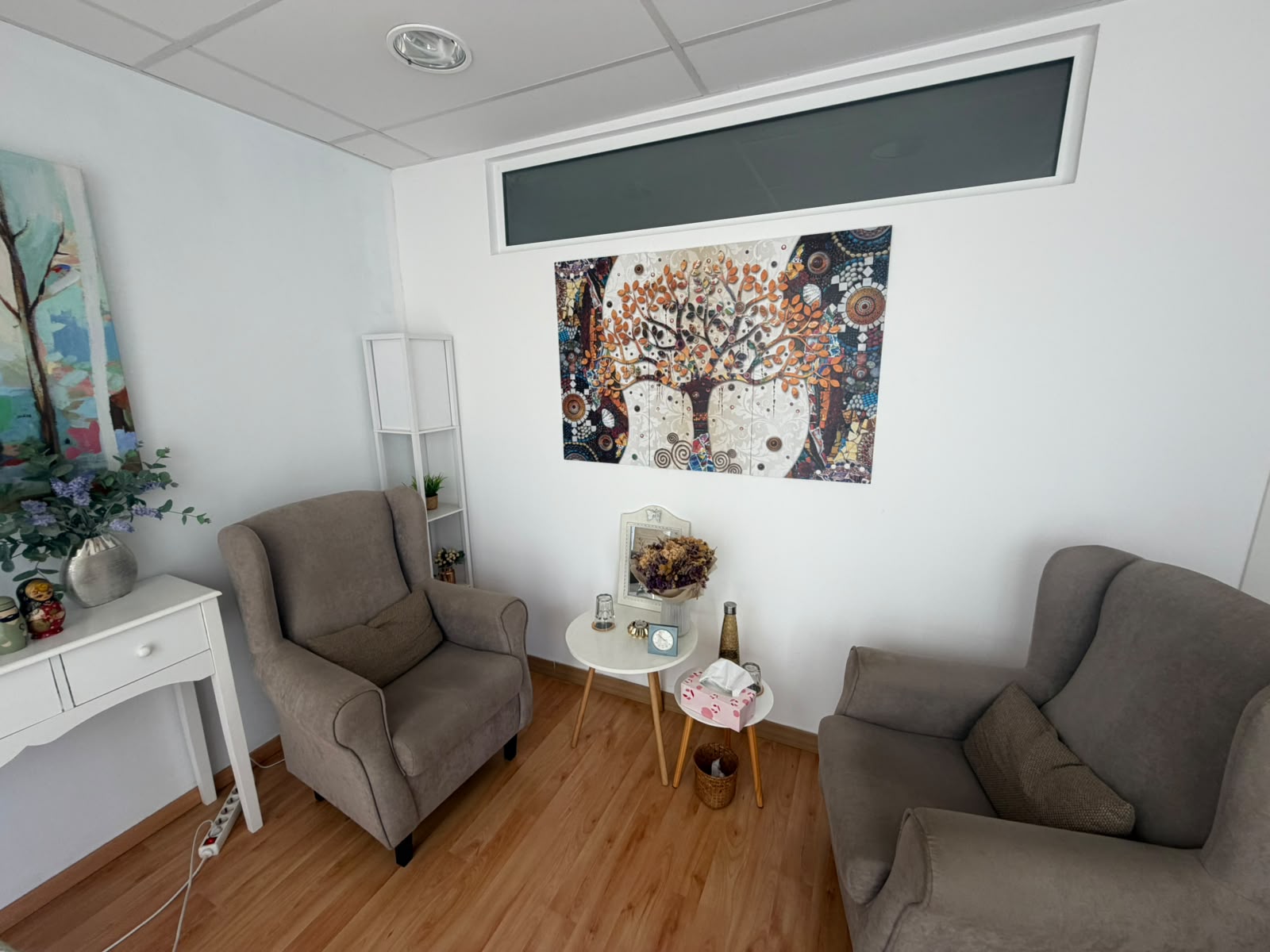 Sala de la consulta de Raquel Turull a Vilassar de Mar, amb dues butaques encarades, una tauleta i un quadre d'un arbre a la paret